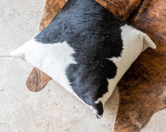 May include: Black and white cowhide pillow with a soft, plush texture. The pillow is made from genuine cowhide and features a unique, natural pattern.