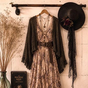 May include: A floral maxi dress with a tiered skirt and lace trim, paired with a dark olive green open-knit cardigan, a brown leather belt, layered necklaces, a black wide-brimmed hat with lace, and brown lace-up leather boots.