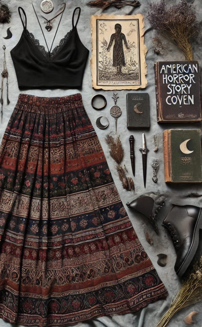 May include: A black lace-trimmed crop top and a long, patterned skirt with red, brown, and blue details are displayed. Accessories include necklaces, rings, a dagger, and books with the title "American Horror Story Coven". Black ankle boots complete the ensemble.