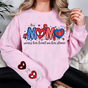 A woman wearing a pink sweatshirt with a Spider-Man design and text on it.