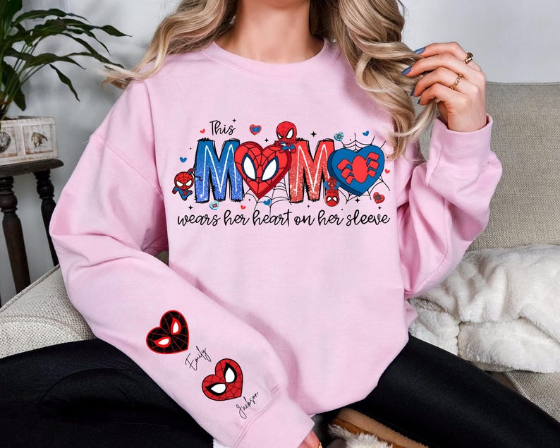 A woman wearing a pink sweatshirt with a Spider-Man design and text on it.