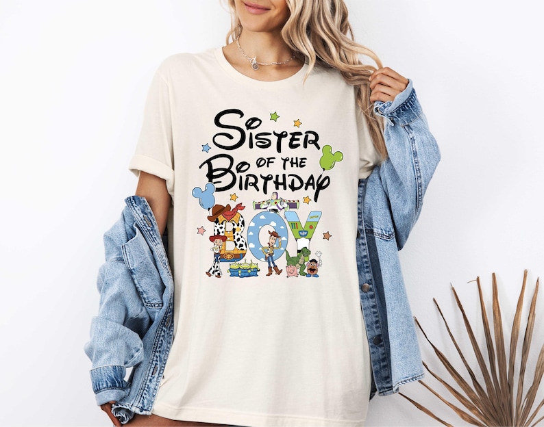 A woman wearing a white t-shirt with a graphic design featuring characters from the Toy Story movie, along with the text "Sister of the Birthday Joy".