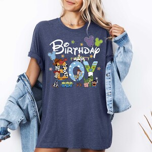 A woman wearing a blue t-shirt with a cartoon character design and the text "Birthday Joy" printed on it.