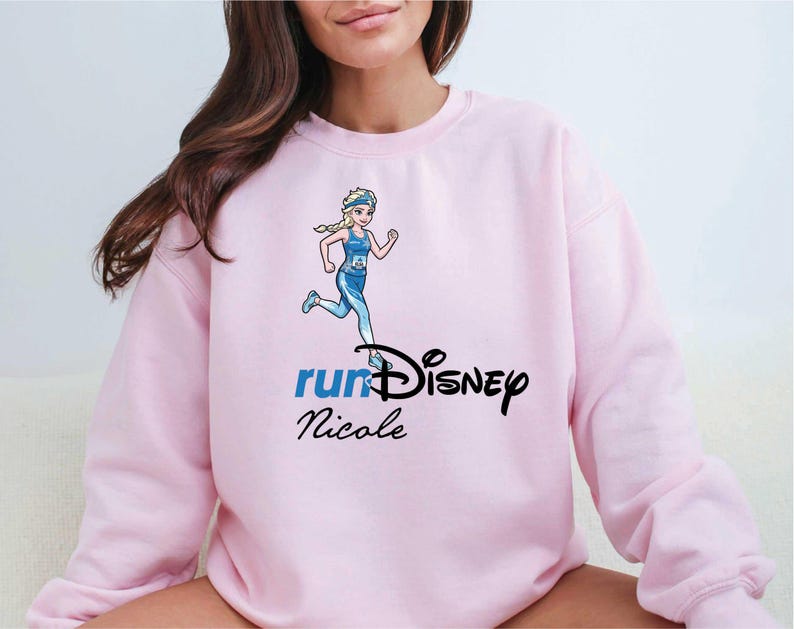 A woman wearing a pink sweatshirt with a Disney-themed graphic and text.