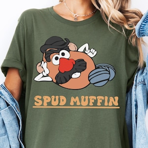 Könnte beinhalten: Ein grünes T-Shirt mit einem Cartoon-Bild von Mr. Potato Head und dem Text "Spud Muffin" auf der Vorderseite.