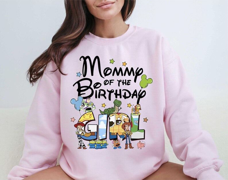 A woman wearing a pink sweatshirt with a cartoon character design and text that says "Mommy of the Birthday Girl".