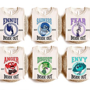Peut inclure: Six t-shirts blancs avec différents personnages et textes d'Inside Out. Chaque t-shirt présente un personnage du film Inside Out, notamment Joie, Tristesse, Colère, Dégoût, Peur et Jalousie. Les t-shirts affichent le texte "Inside Out" et le nom du personnage dans un style vintage.