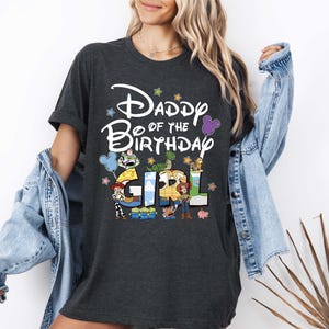 A woman wearing a black t-shirt with a Disney-themed design and text, standing in front of a white wall.