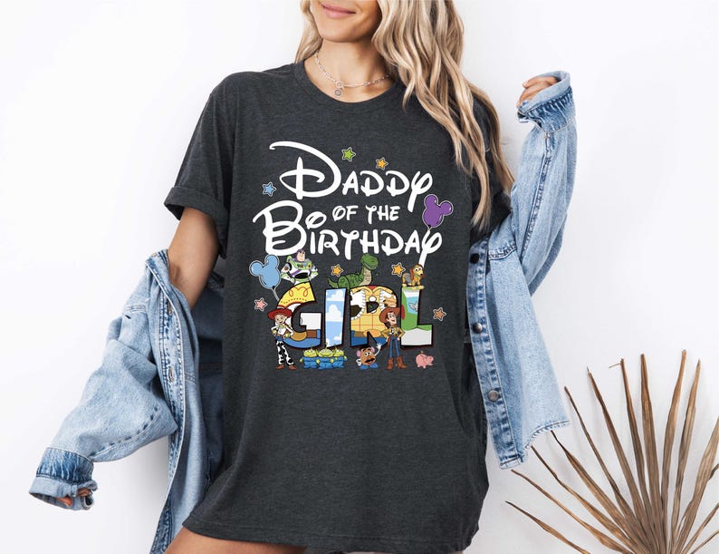 A woman wearing a black t-shirt with a Disney-themed design and text, standing in front of a white wall.