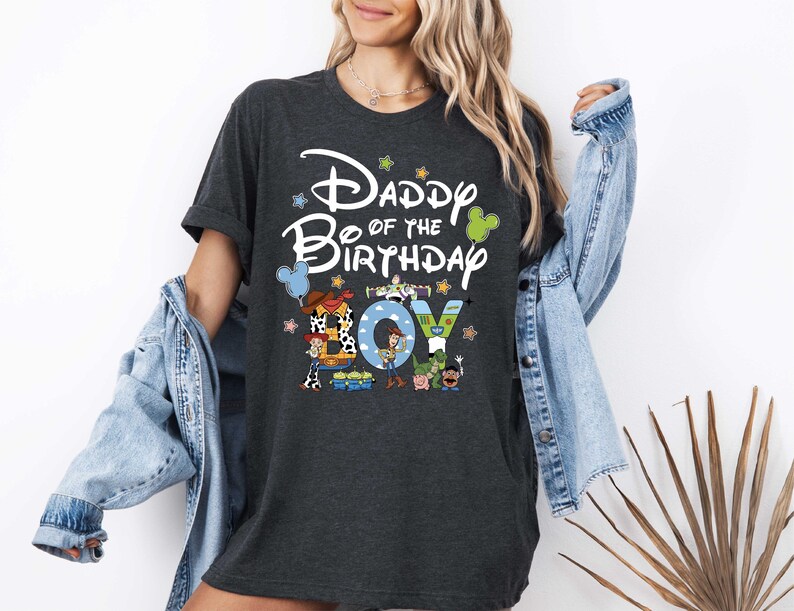 A woman wearing a black t-shirt with a Disney-themed design and text, standing in front of a white wall.