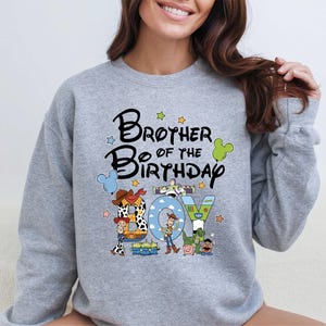 A woman wearing a gray sweatshirt with a cartoon character design and text that says "Brother of the Birthday".
