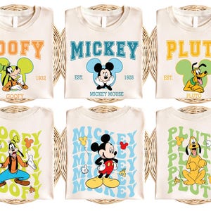 May include: Cream-colored t-shirts featuring cartoon characters Goofy, Mickey Mouse, and Pluto. Each shirt has the character's name in a retro font, with the year of their debut. The shirts are arranged on a woven surface.