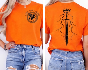 May include: A bright orange short-sleeve t-shirt featuring a black graphic on the front left chest of a winged horse inside a circular border with the text CAMP HALF-BLOOD. The back displays a large black graphic of a sword, crown, and lightning.