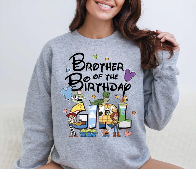 A woman wearing a gray sweatshirt with a colorful graphic design that says "Brother of the Birthday Girl" featuring characters from the Toy Story movie.