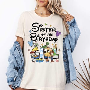 A woman wearing a white t-shirt with a graphic design and text, standing in front of a plant.