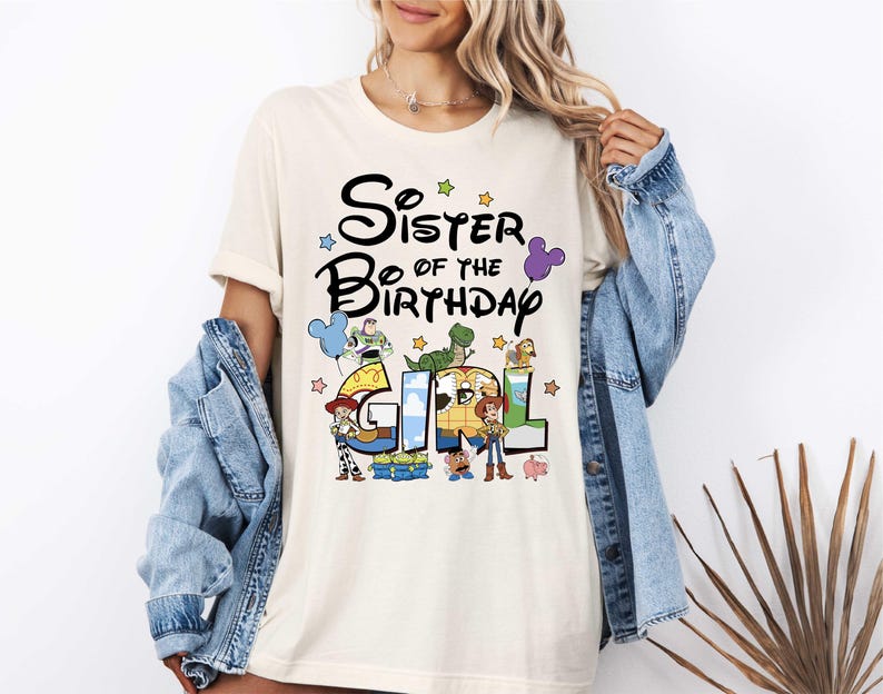 A woman wearing a white t-shirt with a graphic design and text, standing in front of a plant.