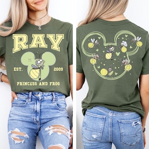 May include: Olive green t-shirt featuring a cartoon firefly design with the text "RAY" in yellow block letters. The shirt also includes the text "EST. 2009 PRINCESS AND FROG". The back of the shirt has a firefly design in a Mickey Mouse shape.