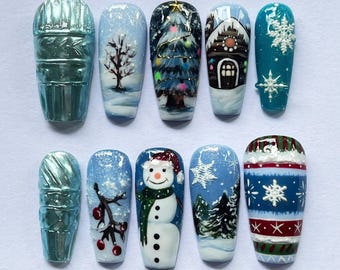 May include: A set of ten artificial nails with winter-themed designs. The designs include a Christmas tree, a snowman, snowflakes, and a gingerbread house, all set against a backdrop of winter landscapes. The nails are painted in shades of blue, white, and green.