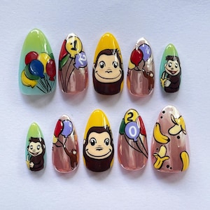 Könnte beinhalten: Ein Satz von zehn mandelförmigen Kunstnägeln mit Cartoon-Designs. Die Designs umfassen einen Affen, Luftballons und Bananen in verschiedenen Farben. Die Nägel haben ein glänzendes Finish und sind auf einer weißen Oberfläche angeordnet.
