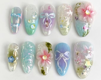 May include: Ten pastel-coloured artificial nails with various designs, including flowers, bows, and glitter. The nails are all oval-shaped and have a glossy finish.
