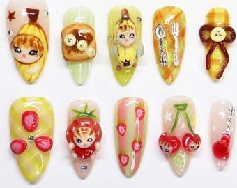 Puede incluir: Un conjunto de diez uñas artificiales con varios diseños temáticos de comida. Las uñas presentan obras de arte detalladas de un gato plátano, tostadas, un gato con traje de plátano, una cuchara y un tenedor, un lazo, fresas, cerezas y una guitarra. Cada uña está pintada con colores brillantes.