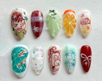 May include: A collection of ten artificial nails with various designs. The designs include cartoon characters, fruit slices, and abstract patterns. Colors include red, green, orange, and white. Some nails feature glitter and star accents.