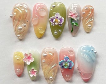 May include: Set of ten false nails with a floral design. The nails are clear with a gradient of color and have different floral designs on each nail. The designs include orchids, swirls, and small flowers.