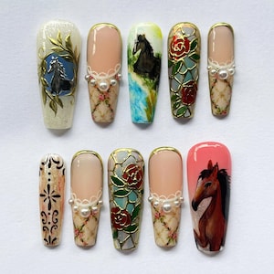May include: A set of ten artificial nails with various designs. The designs include a horse, roses, and floral patterns, with gold accents and pearl embellishments. The nails are painted in shades of pink, beige, and blue.