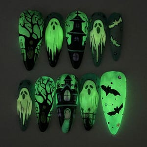 Pode incluir: Um conjunto de dez unhas postiças com tema de Halloween. Os desenhos incluem fantasmas verdes brilhantes, casas assombradas, morcegos e árvores assustadoras em um fundo escuro. As unhas são em forma de amêndoa e brilham no escuro.