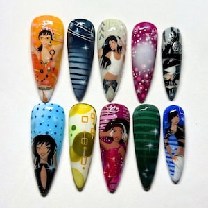 May include: A collection of ten long, almond-shaped artificial nails, each with a unique design. The nails feature cartoon figures, geometric patterns, and abstract art in various colours, with a glossy finish.