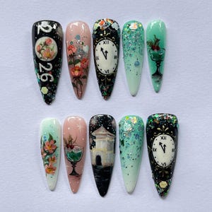 May include: A set of ten long, pointed artificial nails with various designs. The designs include floral patterns, clock faces, glitter, and a building scene. Colors include black, pink, green, and white.