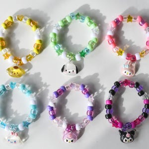 May include: Six colourful beaded bracelets with charms. Each bracelet features a different colour combination and a different cartoon character charm. The charms include a yellow dog, a black and white dog, a pink rabbit, a pink pig, a black cat, and a blue cat.