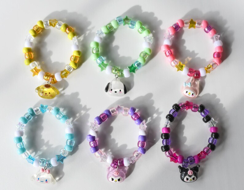 May include: Six colourful beaded bracelets with charms. Each bracelet features a different colour combination and a different cartoon character charm. The charms include a yellow dog, a black and white dog, a pink rabbit, a pink pig, a black cat, and a blue cat.