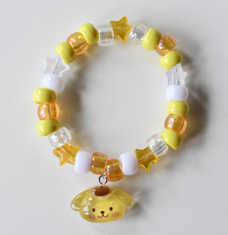 May include: A yellow and white beaded bracelet with star charms and a yellow cartoon dog charm.