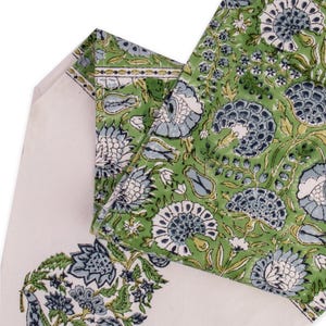 May include: A folded textile featuring a floral pattern in shades of green, blue, and white. The design includes large stylized flowers and foliage. The background is a cream color. The textile is likely a tablecloth or fabric.