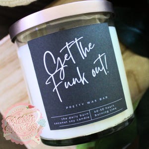 May include: A glass jar candle with a silver lid and a black label. The label reads "Get the Funk out!" in white script. The candle is filled with white wax and is from Pretty Wax Bar.