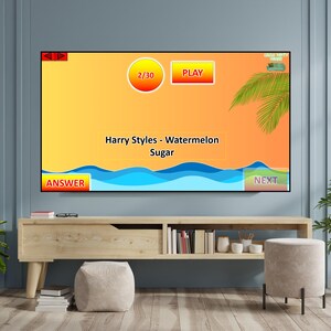 May include: A television screen displays a game interface with the text "Harry Styles - Watermelon Sugar." The screen features a yellow and orange gradient background, blue wave graphics, and various buttons labeled "Answer," "Play," and "Next."