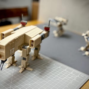 May include: A tan-coloured, four-legged model of a military vehicle with the number 17 on the side. The model has two aerials and two sets of double-barrelled guns. Two additional models are in the background.