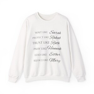 Puede incluir: Una sudadera blanca de manga larga con cuello redondo que presenta el texto en negro: Wait like Sarah, Protect like Rahab, Trust like Ruth, Pray like Hannah, Lead like Esther, Rejoice like Mary. La prenda tiene cuello, puños y dobladillo acanalados.