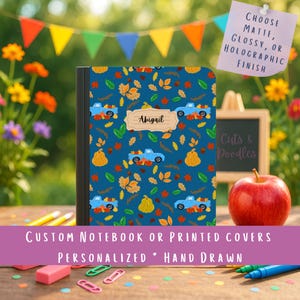May include: A rectangular notebook with a dark blue cover featuring a repeating pattern of light blue pickup trucks, orange pumpkins, and multicolored autumn leaves. A central beige label displays the name Abigail in black cursive script.