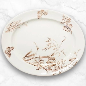 May include: A white oval platter with a brown floral design featuring butterflies, leaves, and stems. The design is reminiscent of a vintage botanical illustration.