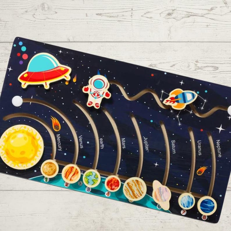 May include: A wooden solar system toy with a blue background and planets in their orbits. The planets are labeled with their names: Mercury, Venus, Earth, Mars, Jupiter, Saturn, Uranus, and Neptune. There is a rocket, an astronaut, and a spaceship on the board.