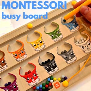 May include: A wooden Montessori busy board featuring cups labelled with colours and numbers. The board includes a magnetic wand and colourful balls. The text "MONTESSORI busy board" is displayed at the top.