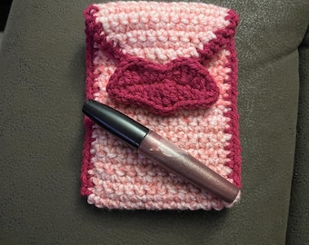 Peut inclure: Une pochette en crochet rose et bordeaux avec un gloss à lèvres à l'intérieur. La pochette a un rabat en forme de cœur.