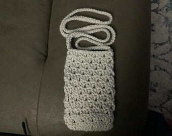 May include: A white crocheted crossbody bag with a long strap. The bag is made with a simple stitch pattern and has a rectangular shape.