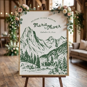 Peut inclure: Un panneau de bienvenue de mariage rectangulaire dans un cadre doré sur un chevalet en bois. Le panneau blanc présente une illustration de chaîne de montagnes vert foncé, des pins et le texte : Welcome to our wedding, Marie & Oliver, September 30, 20xx.