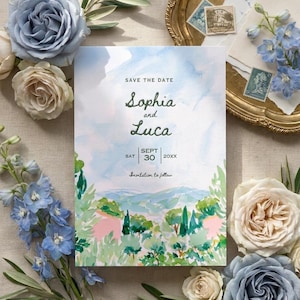 May include: A rectangular Save the Date card featuring a watercolor landscape of rolling hills, trees, and a blue sky. The text reads: SAVE THE DATE, Sophia and Luca, SAT SEPT 30 20XX, and Invitation to follow. The card is surrounded by blue and white roses.