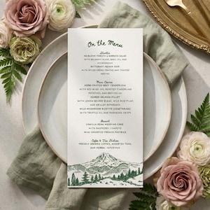 May include: A vertical white menu card with dark green text and a mountain landscape illustration at the bottom. The text reads On the Menu, Starter, Main Course, Dessert, and Coffee & Tea Station, listing various food items and ingredients.