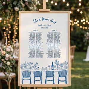 May include: A white wedding seating chart sign in a light wood frame. The text reads Find your Seat, Sophia & Luca, 09.30.XX, Table 1, and Table 2, followed by guest names. A blue line drawing of chairs and table decor sits at the bottom.