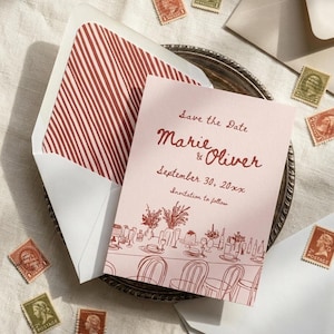 Puede incluir: Una tarjeta Save the Date de color rosa claro con los nombres Marie & Oliver, la fecha 30 de septiembre de 20xx y un dibujo lineal de una mesa de comedor. La tarjeta viene con un sobre que tiene un forro interior de rayas rojas y blancas.